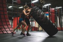 Muscular couple flipping heavy tyre in gym — Stock Photo