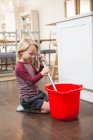 Niño sosteniendo piso fregona con cubo en casa - foto de stock