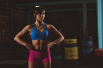 Durchdachte, fitte Frau, die mit den Händen an der Hüfte im Fitnessstudio steht — Stockfoto