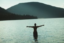 Vista trasera del hombre de pie con los brazos extendidos en un lago - foto de stock