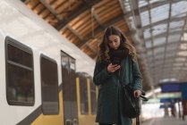 Mujer usando un teléfono móvil en la estación de tren - foto de stock