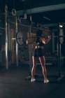 Вид сзади на здоровую женщину, поднимающую штангу в спортзале — стоковое фото