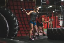 Muskulöses Paar schlägt mit Vorschlaghammer in Turnhalle auf Reifen ein — Stockfoto