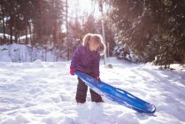 Menina bonito segurando trenó na neve durante o inverno — Fotografia de Stock
