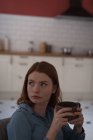Задумчивая молодая женщина держит кофейную кружку дома — стоковое фото