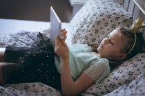 Девочка с цифровым планшетом на кровати в спальне — стоковое фото