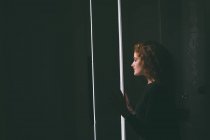 Задумчивая женщина смотрит в окно на дом — стоковое фото