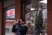 Чоловік натискає фотографію з цифровою камерою за межами магазину — стокове фото