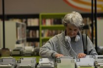 Mulher sênior escolhendo uma fita cassete de DVD na biblioteca — Fotografia de Stock