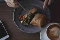 Primer plano de la mujer que tiene comida con cuchara y tenedor en la cafetería - foto de stock