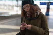 Жінка в зимовому одязі, використовуючи мобільний телефон на залізничній станції — стокове фото