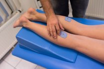 Физиотерапевт накладывает подушечки на женские ноги в клинике — стоковое фото