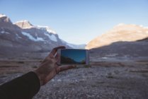 Homem tirando fotos de montanhas com telefone celular em um dia ensolarado — Fotografia de Stock