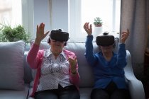 Amigos seniores usando fones de ouvido de realidade virtual em casa — Fotografia de Stock