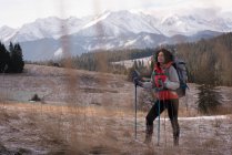 Donna premurosa in piedi con zaino e palo da trekking durante l'inverno — Foto stock