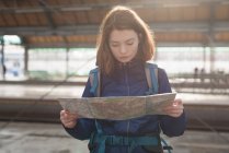 Женщина-путешественница с рюкзаком смотрит на карту в ожидании поезда — стоковое фото