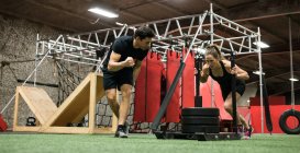Treinador ajudando mulher com trenó empurrando no estúdio de fitness — Fotografia de Stock