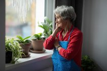 Ragionevole donna anziana guardando attraverso la finestra a casa — Foto stock