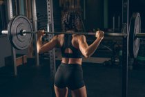 Vue arrière de la femme en forme soulevant la barre dans la salle de gym — Photo de stock