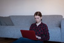 Jeune femme utilisant un ordinateur portable dans le salon à la maison — Photo de stock