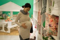 Счастливая беременная женщина прикасается к животу во время покупок — стоковое фото
