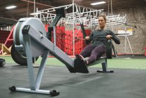 Muscular woman exercising on rowing machine at gym — Stock Photo