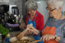 Amigos seniores cozinhar alimentos juntos na cozinha em casa — Fotografia de Stock