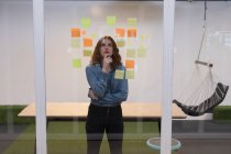 Задумчивая женщина-руководитель читает липкие заметки на стекле в офисе — стоковое фото