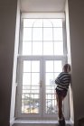 Вид ззаду вдумливої жінки, яка дивиться через вікно вдома — стокове фото