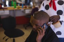 Cliente che parla al cellulare mentre il barbiere si taglia i capelli in barbiere — Foto stock