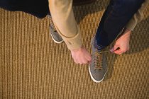 Низкая часть человека завязывая шнурки в гостиной на дому — стоковое фото