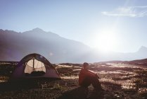 Задумчивый человек сидит возле палатки в солнечный день — стоковое фото