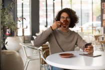 Junger Mann trinkt Kaffee, während er Handy in Restaurant benutzt — Stockfoto