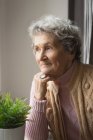 Задумчивая пожилая женщина улыбается дома — стоковое фото