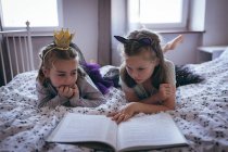 Sisters reading a book on bed in bedroom — Stock Photo