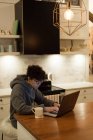 Bella donna che utilizza il computer portatile mentre prende il caffè in cucina — Foto stock