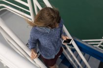 Высокий угол обзора женщины с помощью мобильного телефона на лестнице круизного лайнера — стоковое фото
