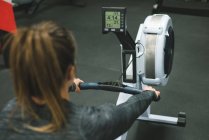 Visão traseira da mulher muscular se exercitando na máquina de remo no ginásio — Fotografia de Stock