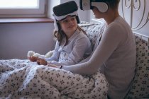 Mère et fille interagissent en utilisant un casque de réalité virtuelle sur le lit — Photo de stock