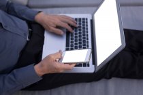 Seção média do homem de negócios usando telefone celular enquanto trabalhava no laptop — Fotografia de Stock