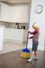 Мальчик чистит пол метлой на кухне дома — стоковое фото