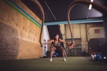 Mujer en forma haciendo ejercicio de cuerda de batalla en el gimnasio - foto de stock