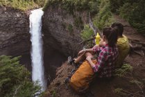 Casal sentado perto de cachoeira em um dia ensolarado — Fotografia de Stock