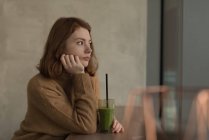 Mujer reflexiva teniendo salud sacudida bebida en la cafetería - foto de stock