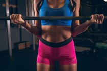 Partie médiane de la femme en forme soulevant la barre d'haltère dans la salle de gym — Photo de stock
