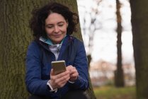 Молода жінка використовує мобільний телефон у парку — стокове фото