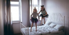 Irmãs de traje brincando na cama no quarto — Fotografia de Stock