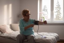 Старшая женщина проверяет кровяное давление на мониторе дома — стоковое фото