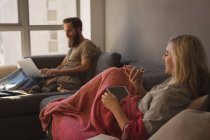 Жінка розмовляє на мобільному телефоні, коли чоловік використовує ноутбук у вітальні вдома — стокове фото