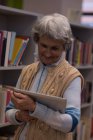 Active senior woman using digital tablet in library — Stock Photo